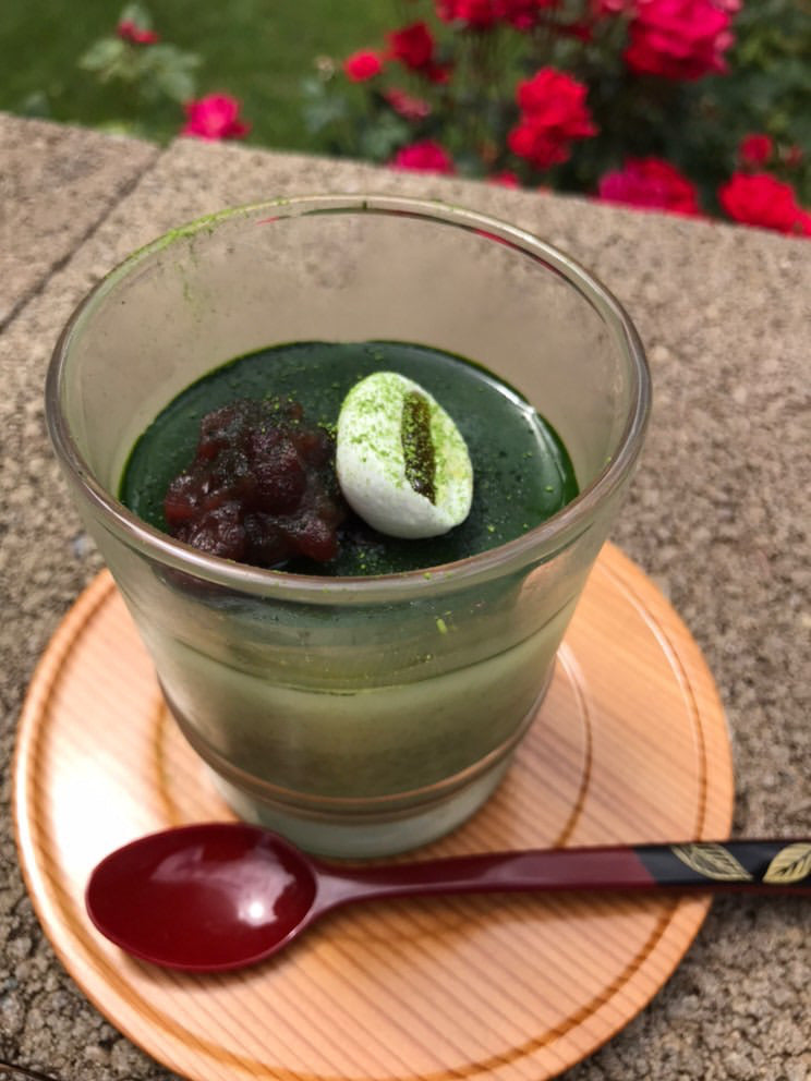 bright green matcha panna cotta in a glass cup sitting on a wooden coaster with a wooden spoon