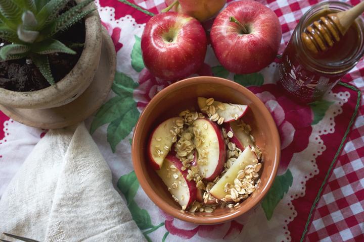 bowl of apples with granola and honey next to apples and a jar of honey with a wooden dipper