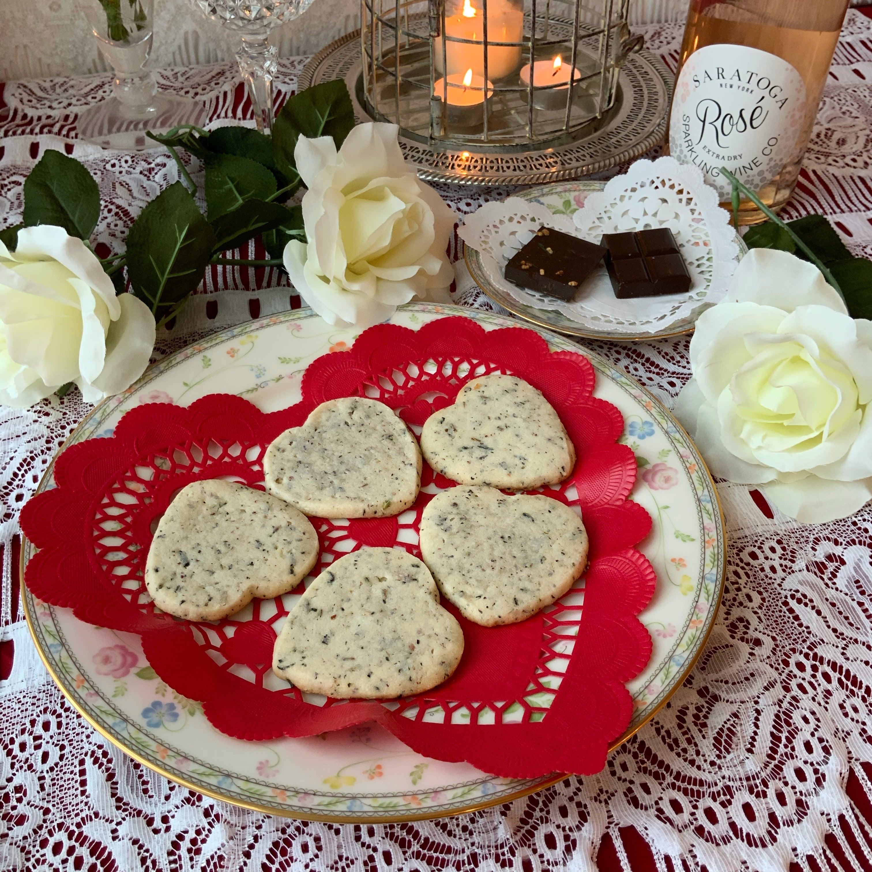 plate with a red heart doily and five heart shaped shortbread cookies next to roses and a candle centerpiece