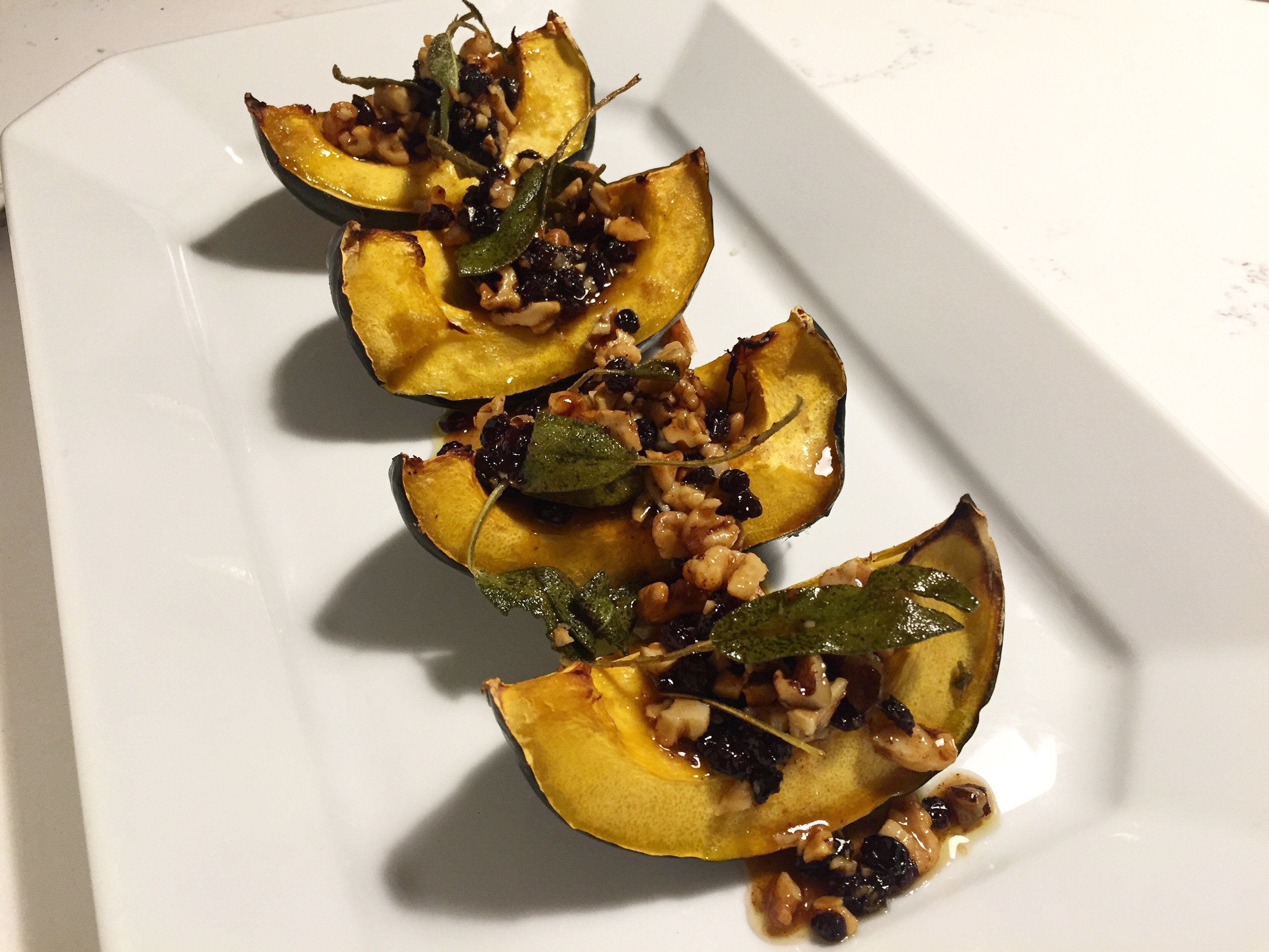 diagonal line of four roasted and stuffed acorn squash wedges on a white plate