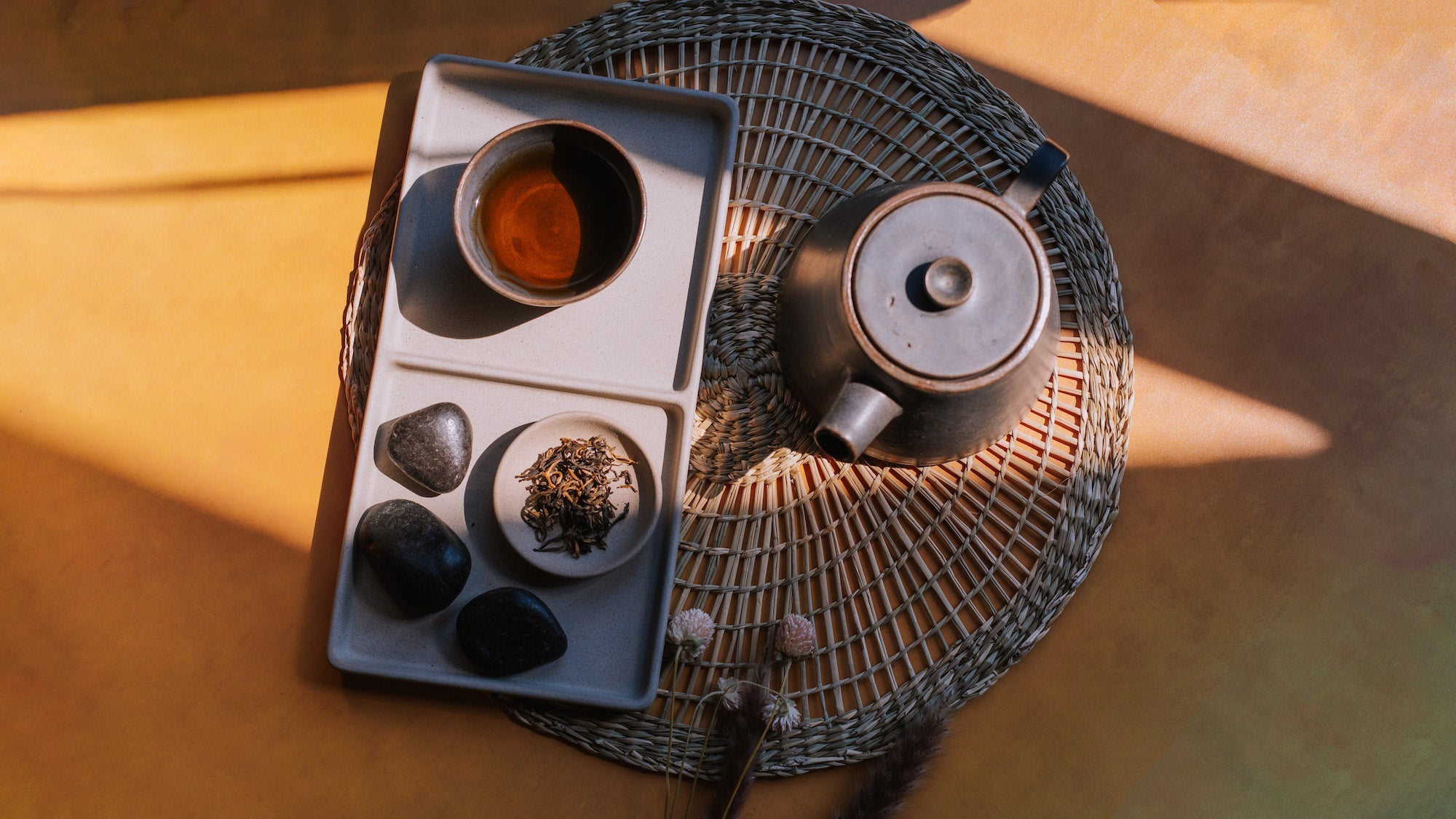 aerial view of black tea in a minimalist cup on a stone tray with a small dish of loose leaf black tea next to a minimalist rustic teapot