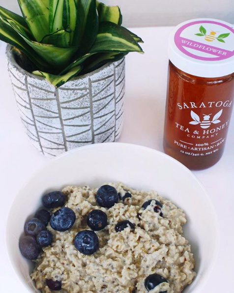 white bowl of oatmeal with blueberries and a jar of local wildflower honey