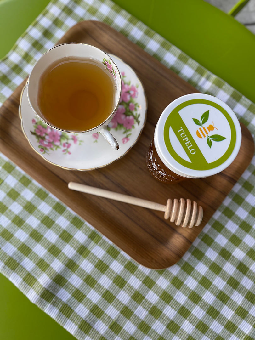 a cup of tea in a white and pink floral vintage tea cup set on a wooden tray next to a honey dipper and a jar of tupelo honey