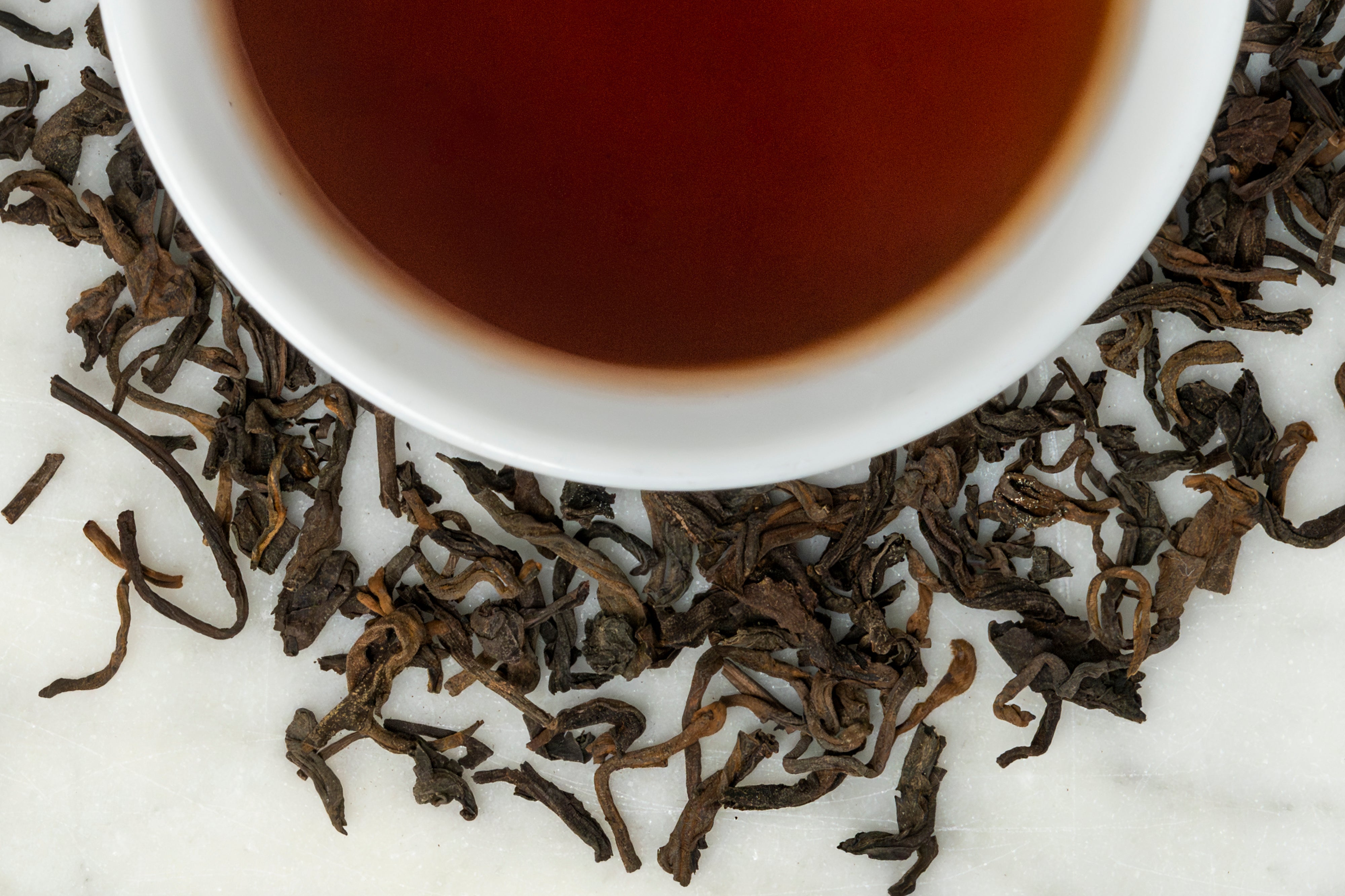 cup of 2016 Jingmai shou pu erh with loose leaf tea leaves around the cup