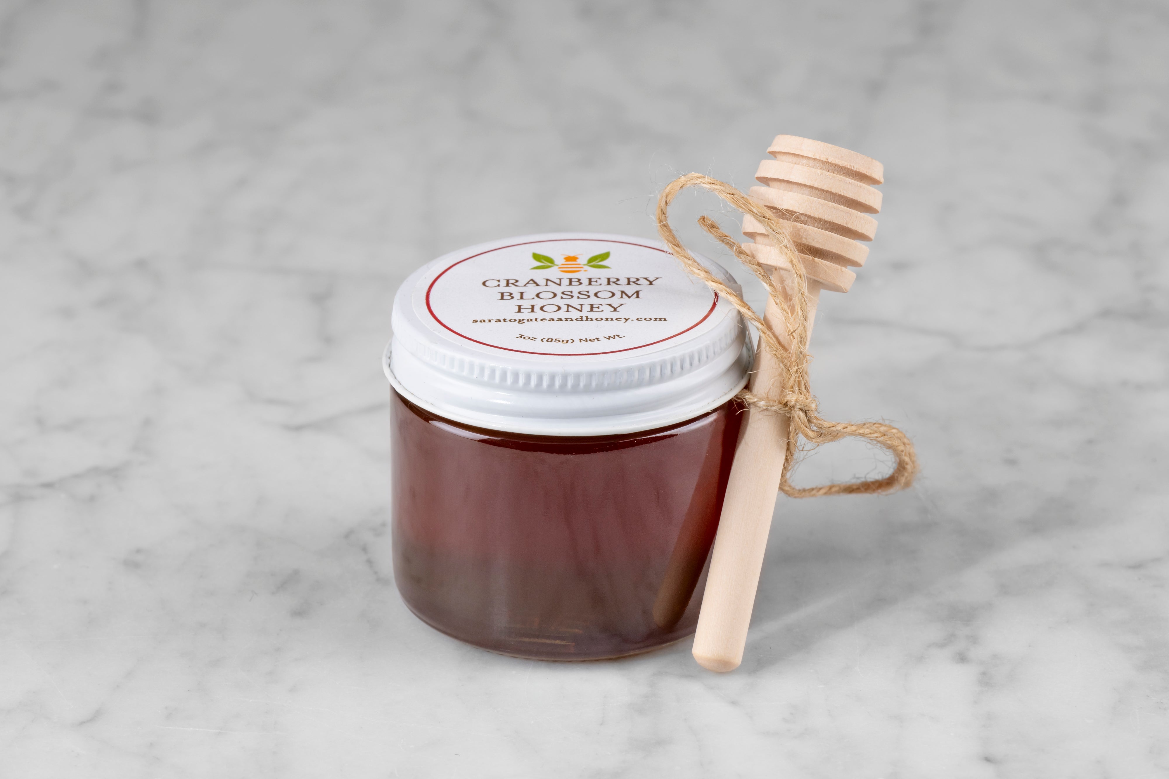 3oz jar of Cranberry Blossom Honey with twine and mini dipper on a marble background