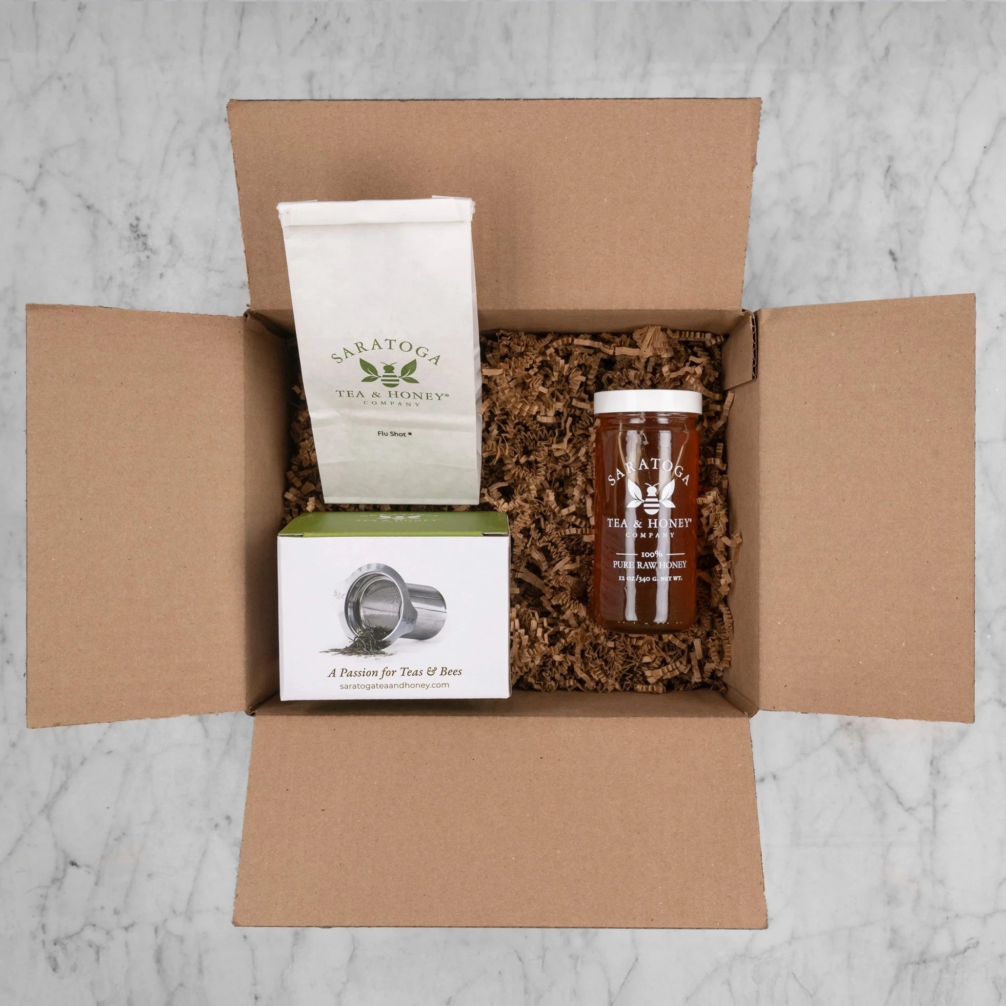 showing gift set contents option 1 in brown box with gift fill: 2oz bag of tea, stainless steel tea infuser, and jar of elderberry honey