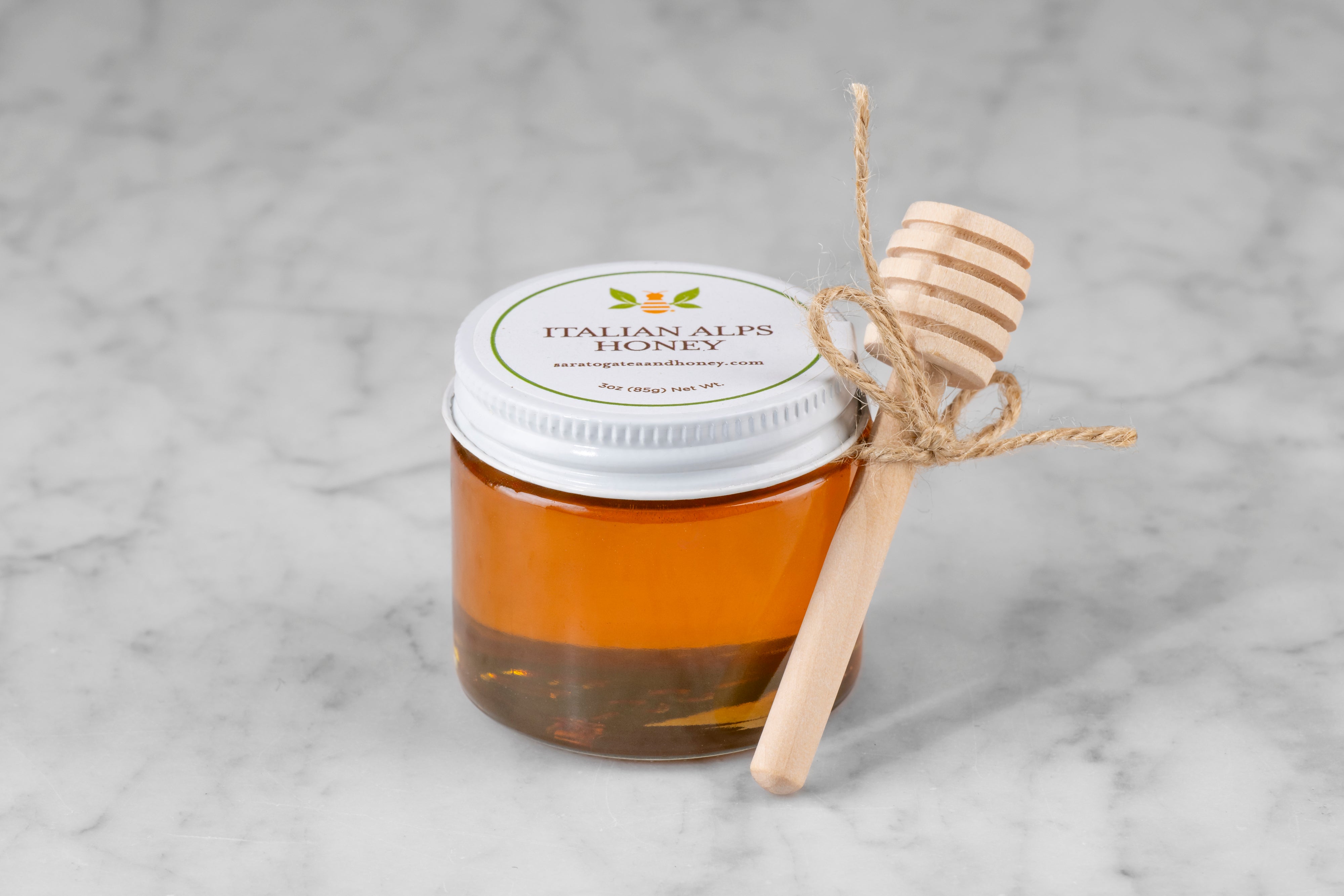 3oz jar of Italian Alps Honey with twine and mini dipper on a marble background