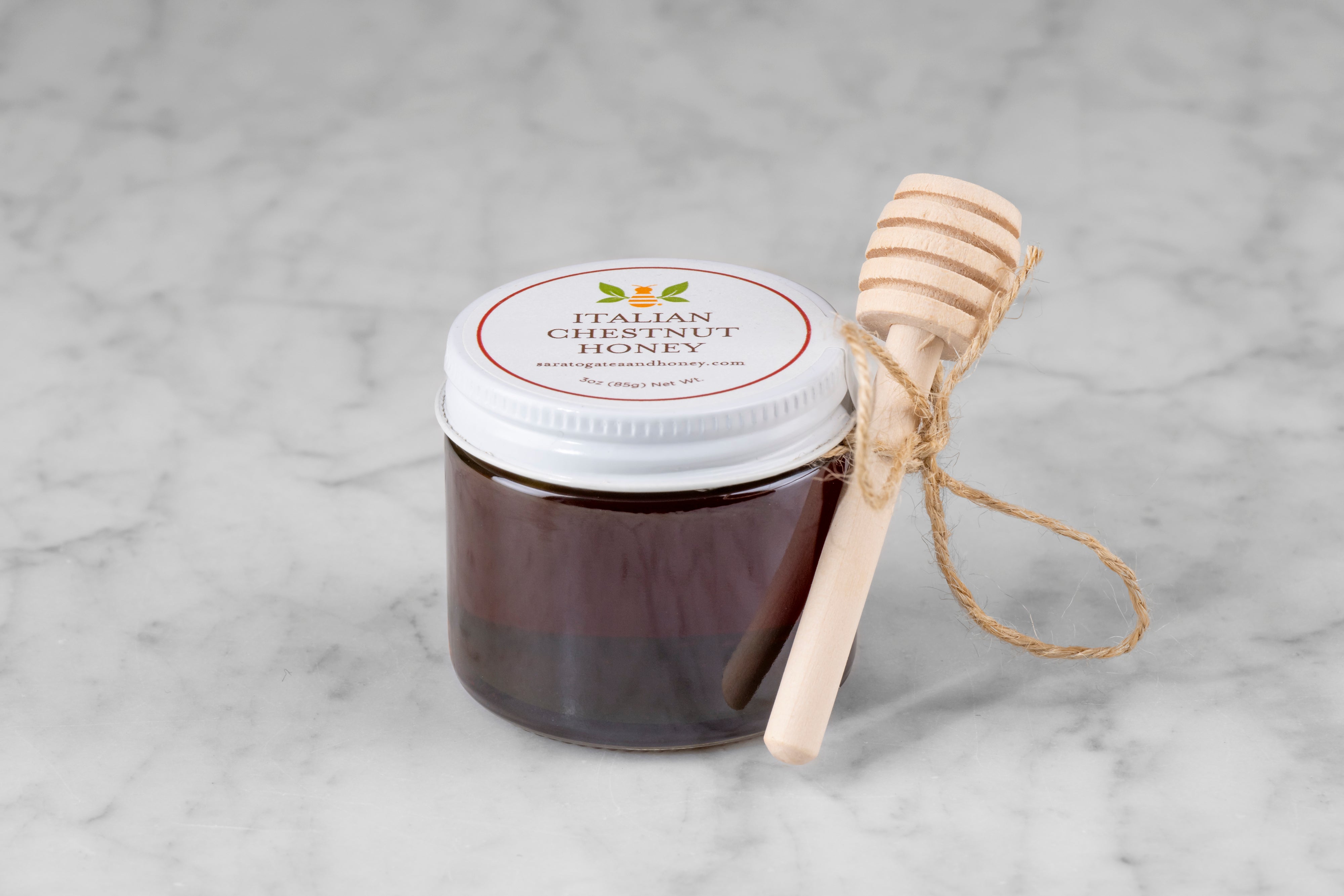 3oz jar of Italian Chestnut Honey with twine and mini dipper on a marble background