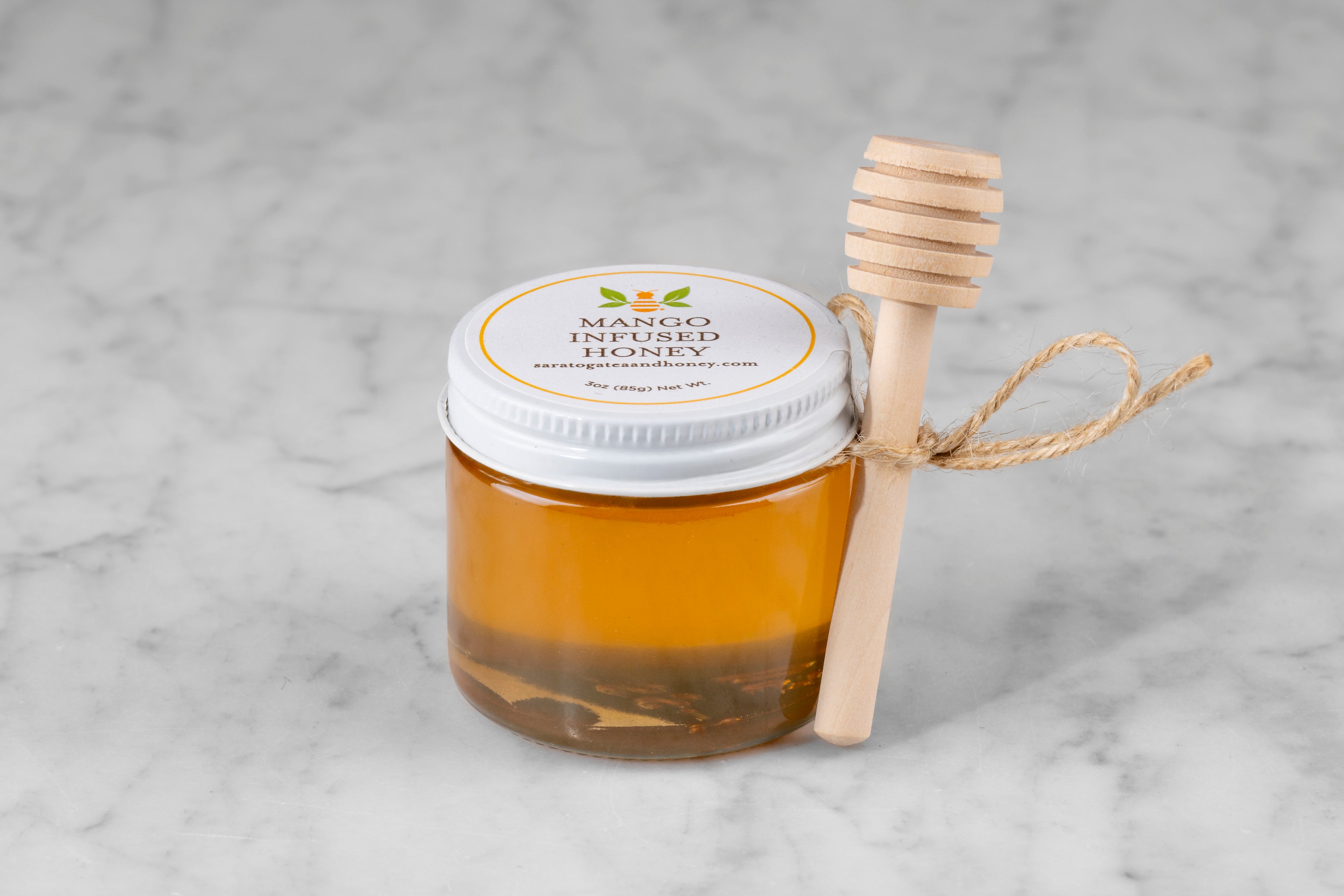 3oz jar of Mango Infused Honey with twine and mini dipper on a marble background