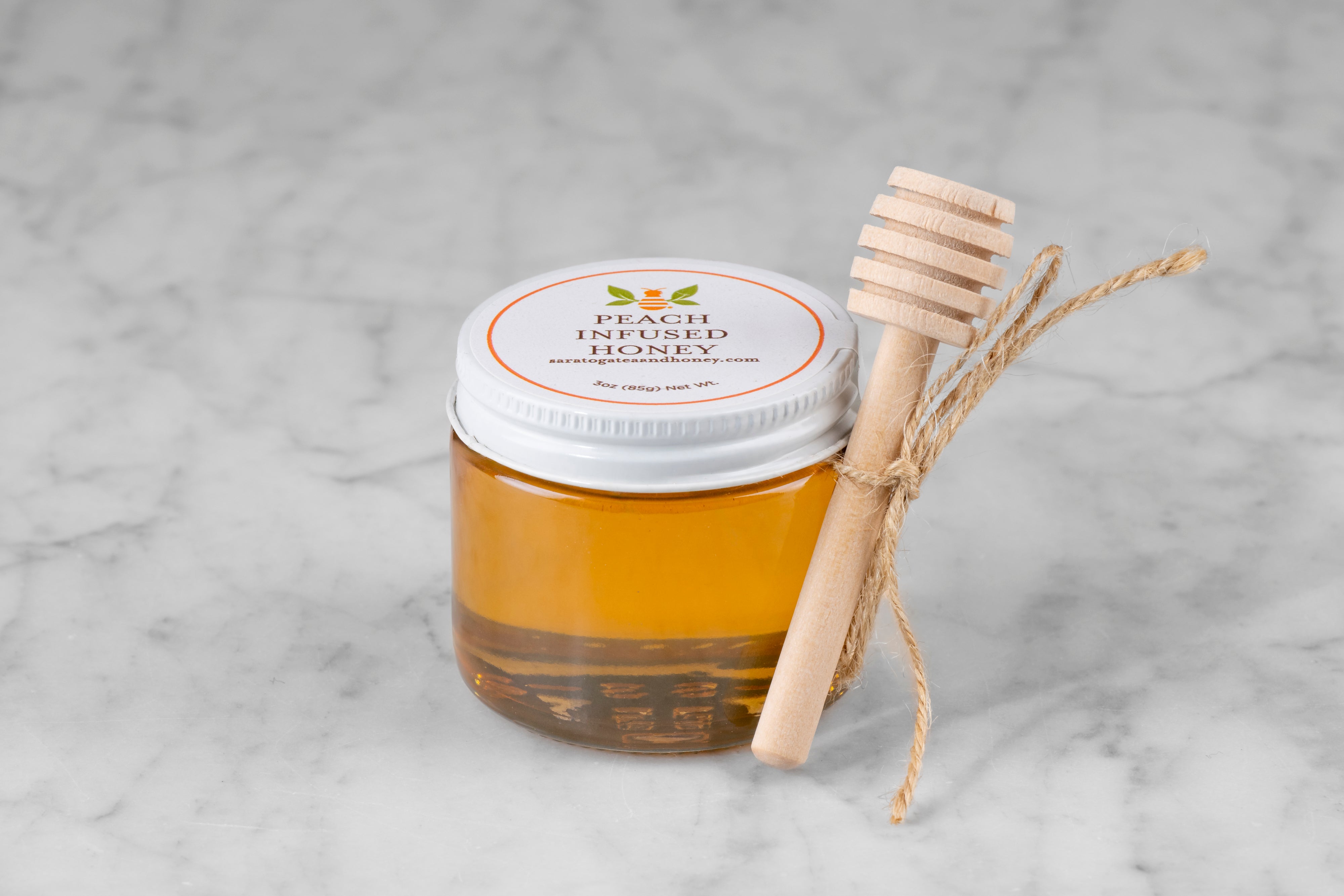 3oz jar of Peach Infused Honey with twine and mini dipper on a marble background