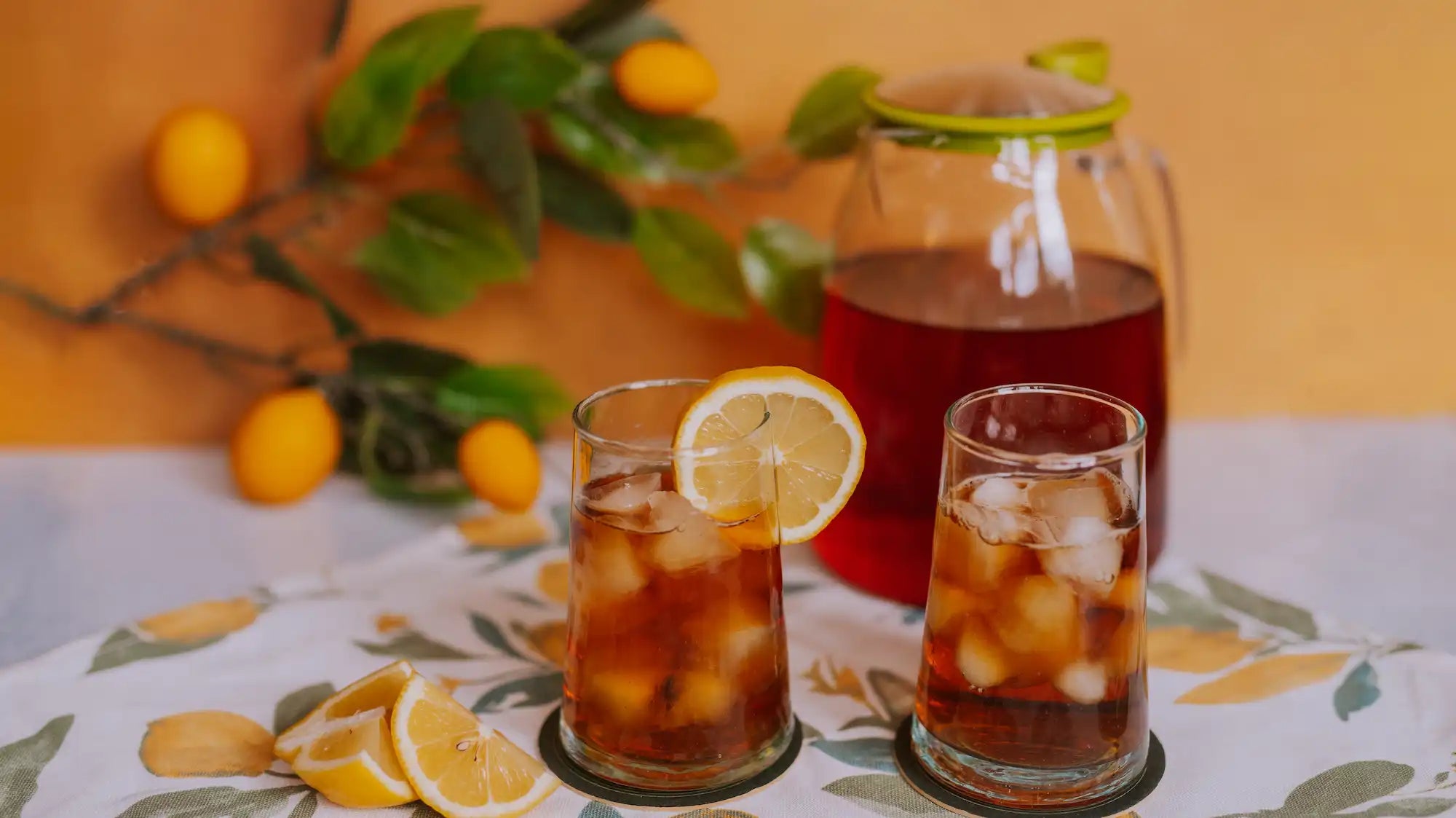 two glasses of iced black tea with a slice of lemon and a pitcher of iced black tea