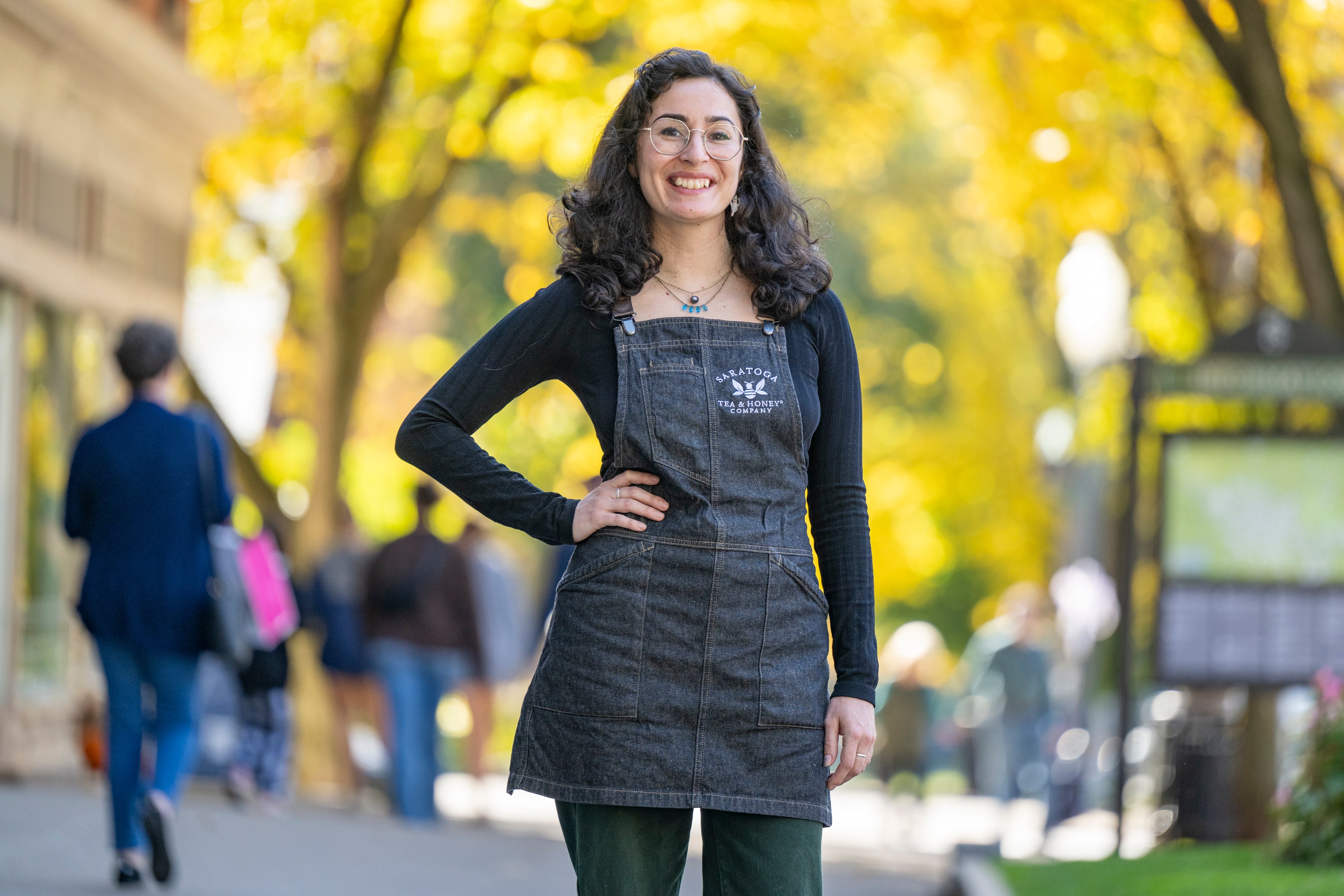 woman with black hair wearing a denim Saratoga Tea & Honey Co. apron on Broadway in Saratoga Springs NY