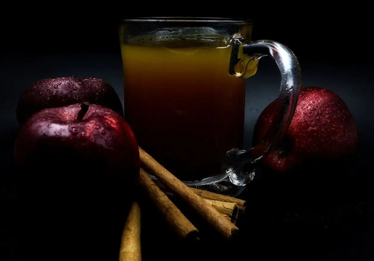 apples surrounding a cup of apple cider with cinnamon sticks