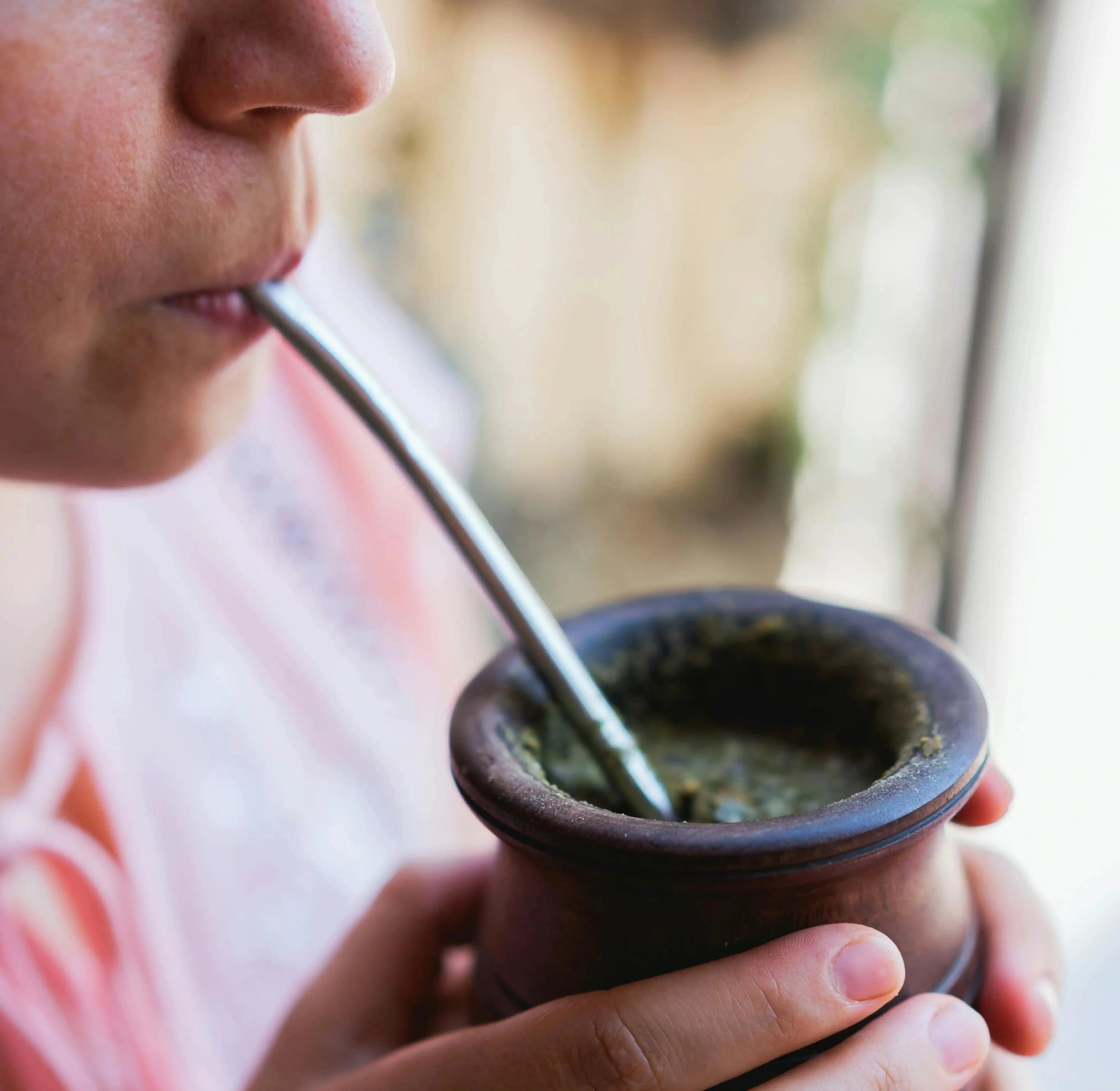 woman in pink shirt drinking yerba mate out of a gourd through a bombilla (metal straw)