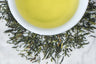 loose leaf sencha surrounding a white cup with brewed green tea