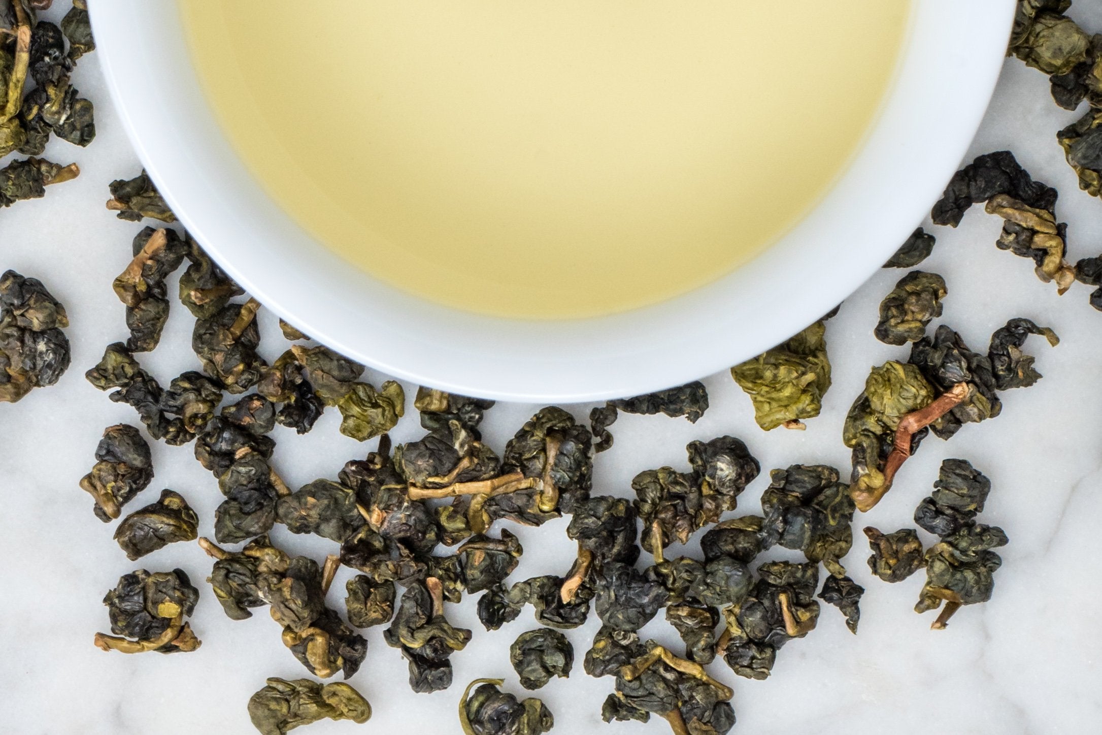 loose leaf high mountain rolled oolong Shan Lin Xi surrounding a white cup with brewed tea