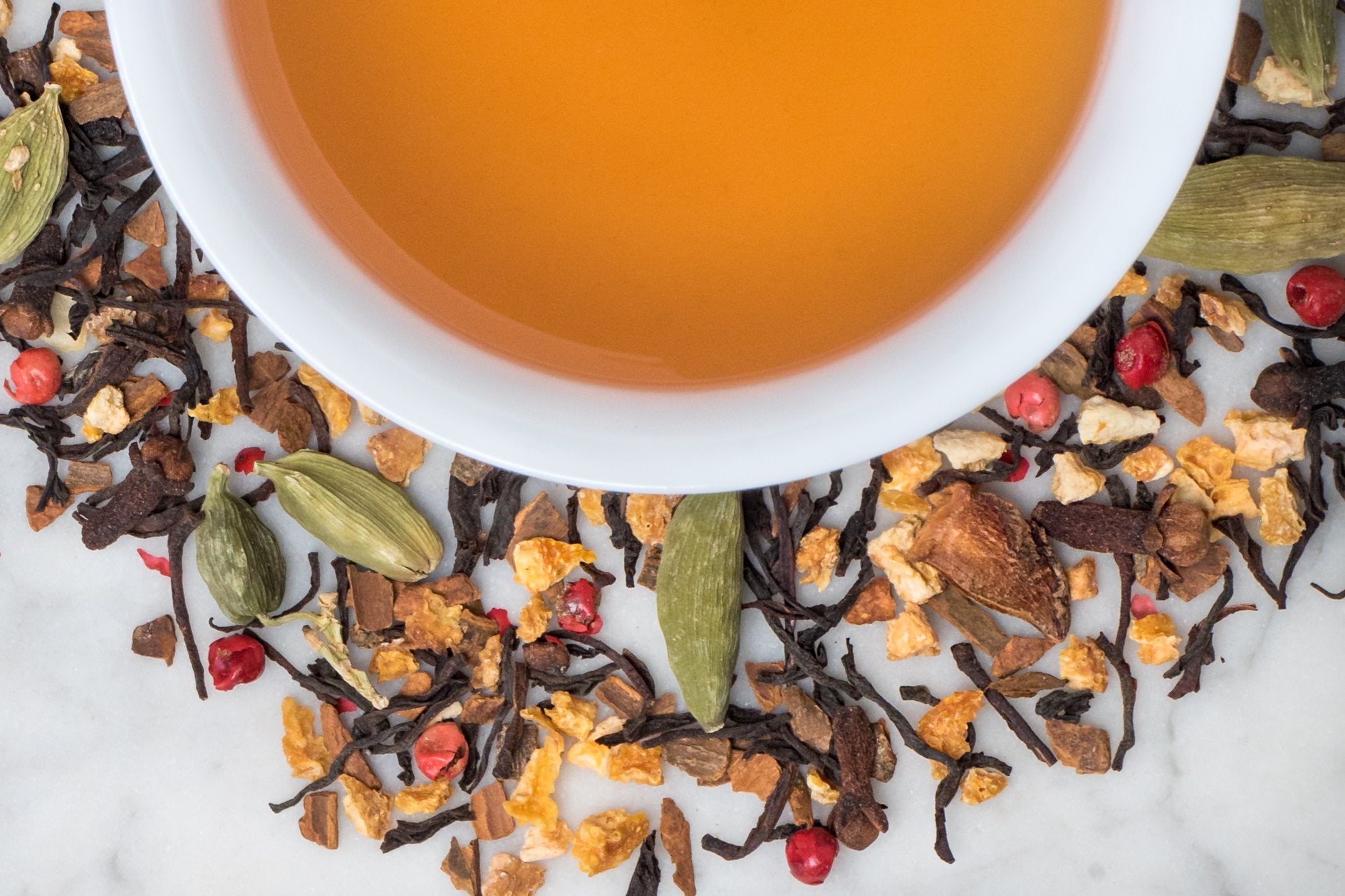 loose leaf spiced orange chai surrounding a white cup with brewed tea