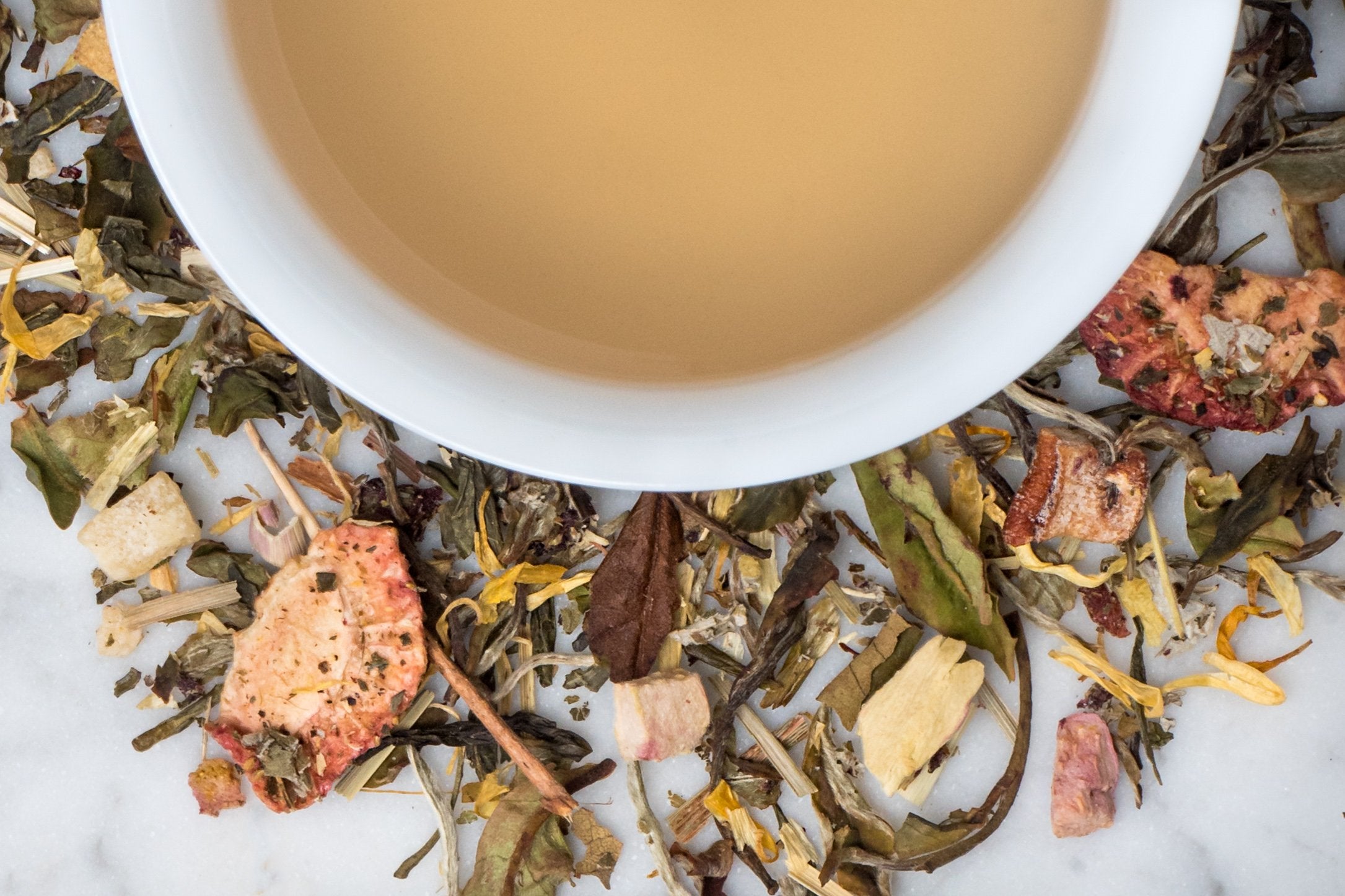 loose leaf strawberry green tea surrounding a white cup of brewed tea