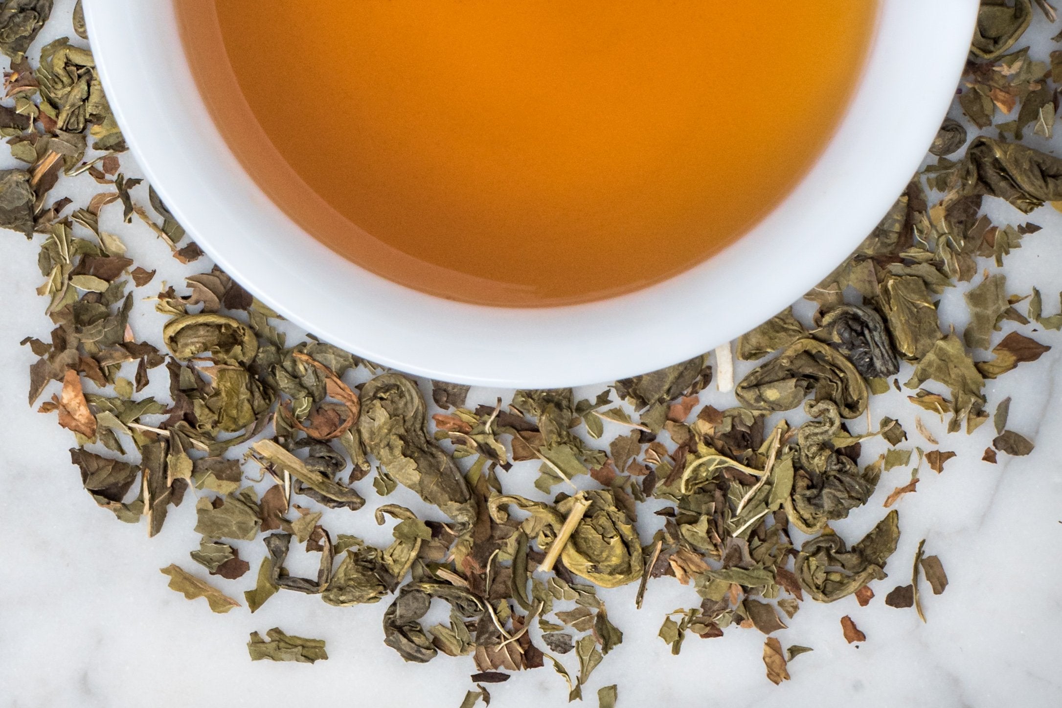 loose leaf moroccan mint green tea surrounding a white cup with brewed tea